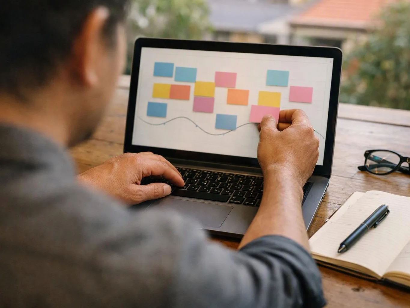 A person works on a laptop, moving colourful sticky notes across a chart on the screen